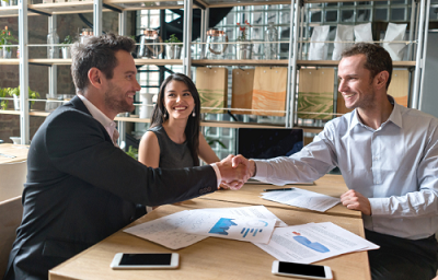 3 office wrokers smile as they sit across from each other in a meeting