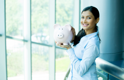 Woman stands, smiling as she holds a piggy bank